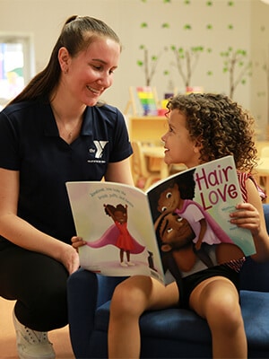 Girl reading book next to YMCA team member / Career with a Cause image